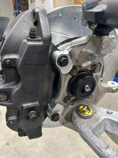 Rear view of a Brembo-style brake caliper mounted to an aluminum spindle with a sealed hub and slotted brake rotor.