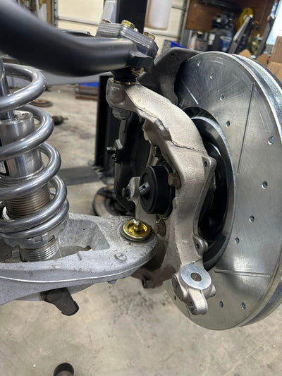 Front suspension assembly featuring adjustable coilovers, tubular control arms, and a slotted disc brake rotor on a performance spindle.