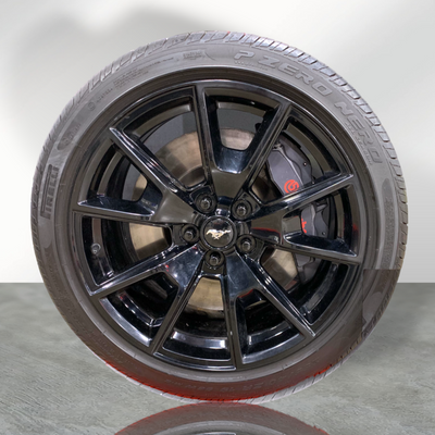 Close-up of a black multi-spoke Ford Mustang wheel featuring a Pirelli P Zero Nero tire and a grey Brembo brake caliper over a ventilated disc rotor.